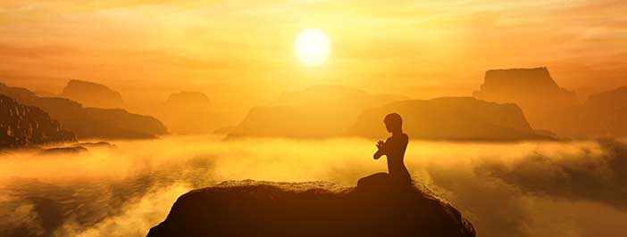 Woman meditating atop a cloudy mountain during sunset